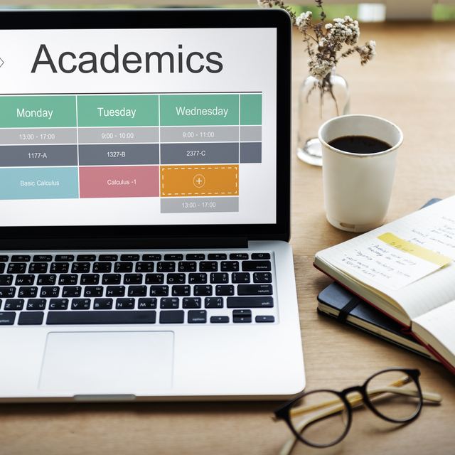 A class timetable open on a laptop beside a notebook and a cup of coffee.